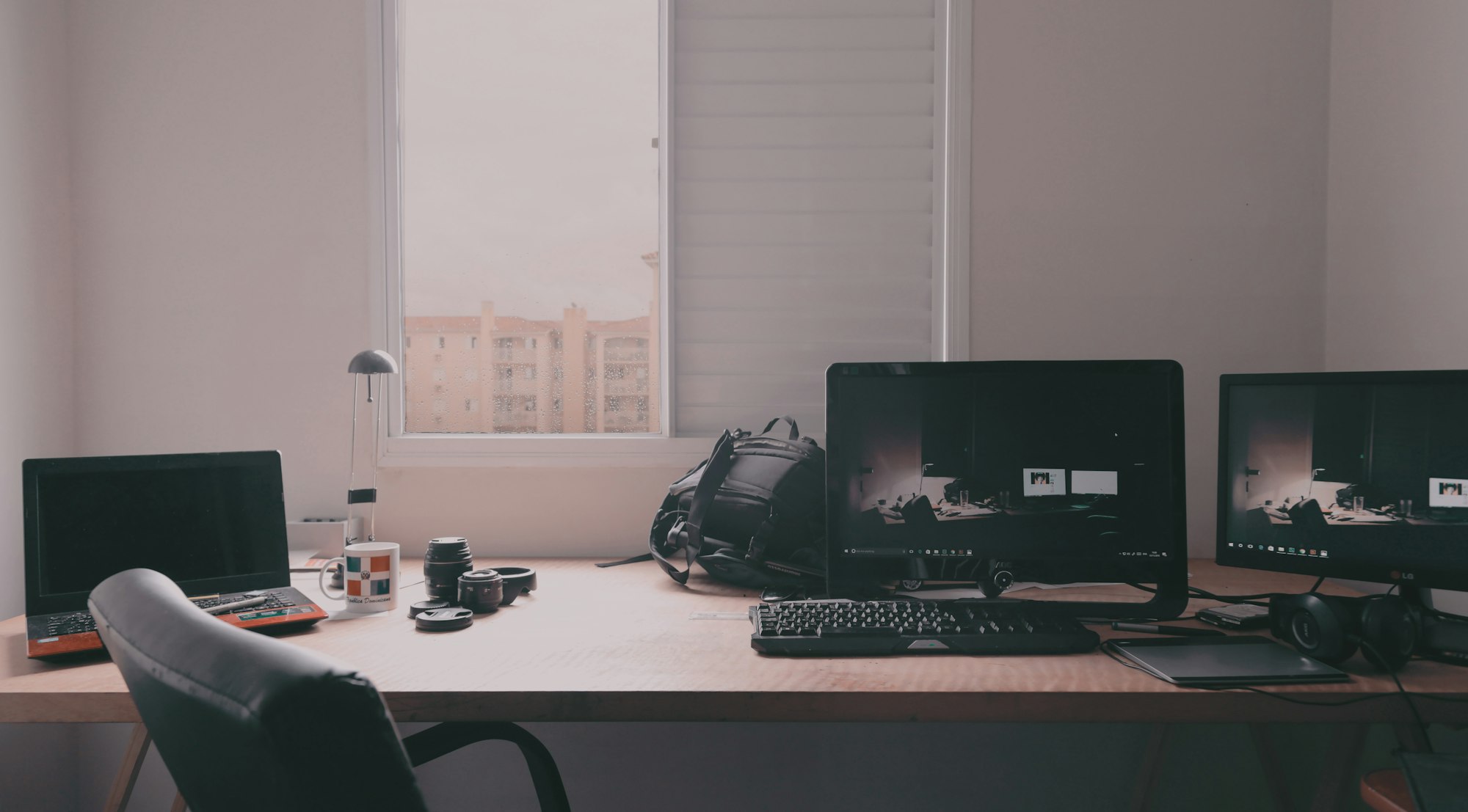 Minimal workspace with a single monitor and keyboard on a wooden table by a window.